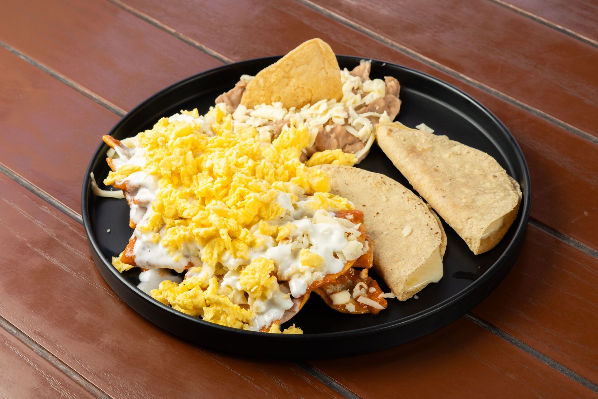 Delicious Mexican breakfast platter featuring chilaquiles, scrambled eggs, and tortillas on a black plate.